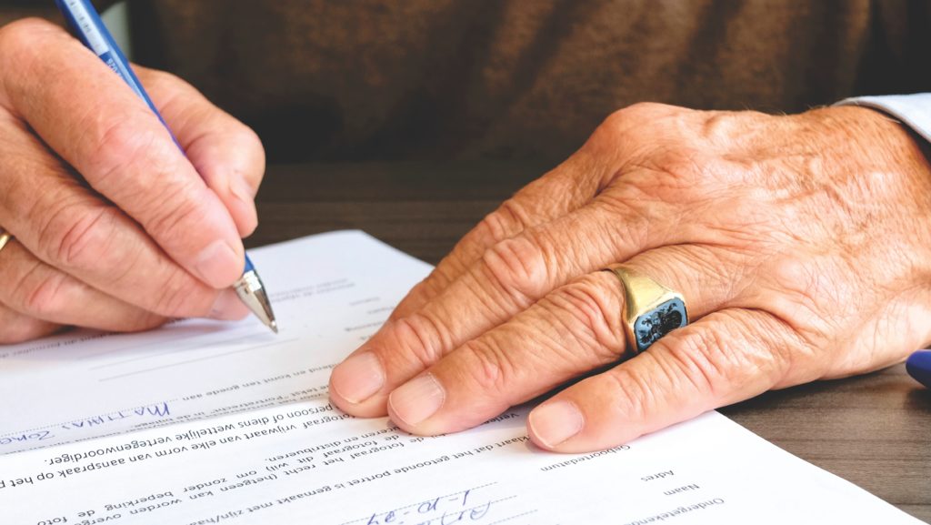 An elderly man signs for power of attorney